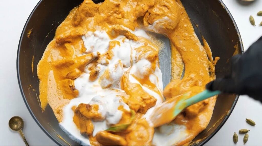 Adding fresh cream Fresh cream being added to creamy butter chicken sauce and gently stirred before simmering.