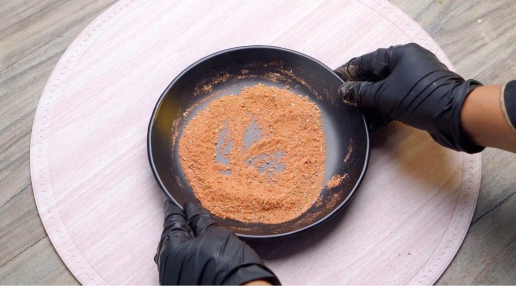 Cajun seasoning A small glass bowl filled with vibrant red-orange Cajun seasoning, surrounded by scattered whole spices like peppercorns, dried chili flakes, and a dusting of paprika on a rustic wooden surface.