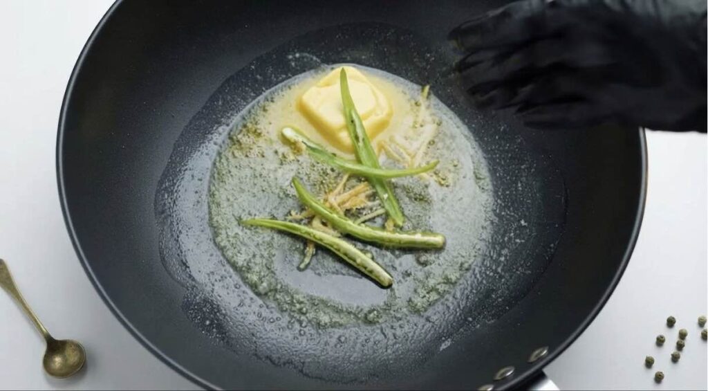 Cook the butter and ginger Melted butter sizzling with julienned ginger, green chilies, and a pinch of red chili powder in a pan.
