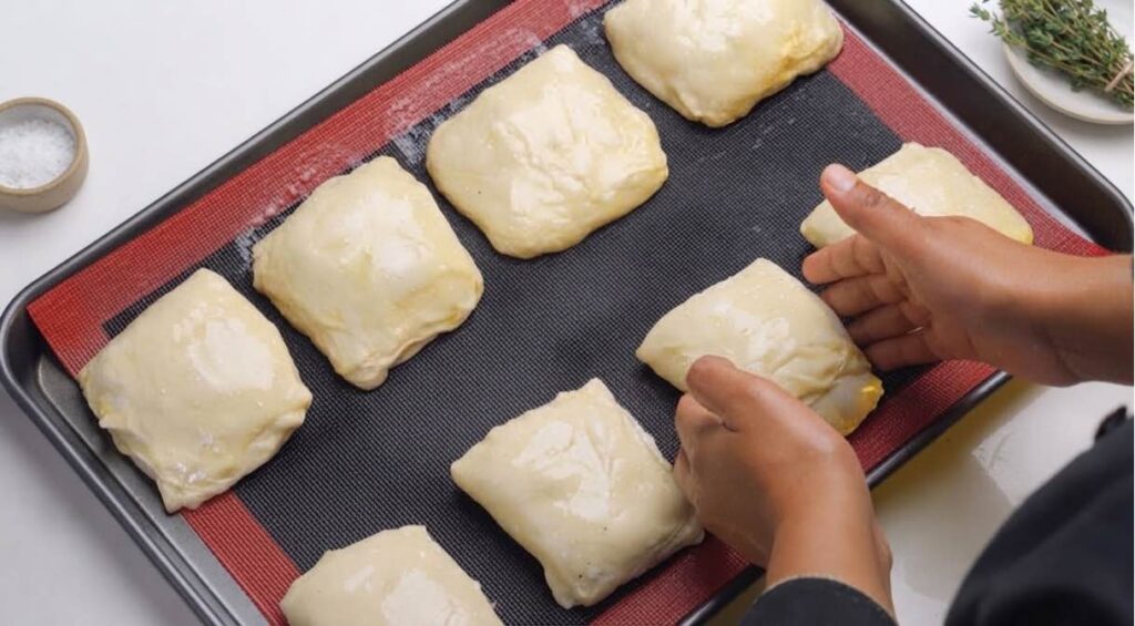 Turkish borek Shaped chicken börek rolls brushed with egg yolk arranged on a parchment-lined baking tray