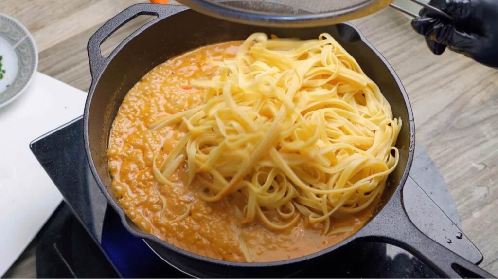 Add the fettuccine Cooked fettuccine being added to the creamy Cajun sauce in a hot skillet, ready to be tossed together.